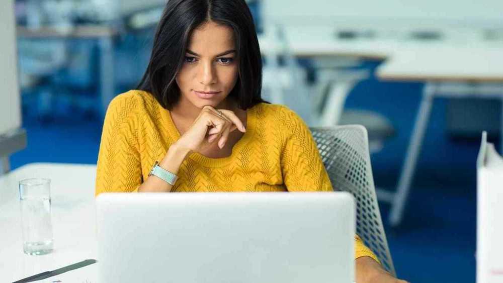 Mujer mirando su computadora con la mano en la barbilla.